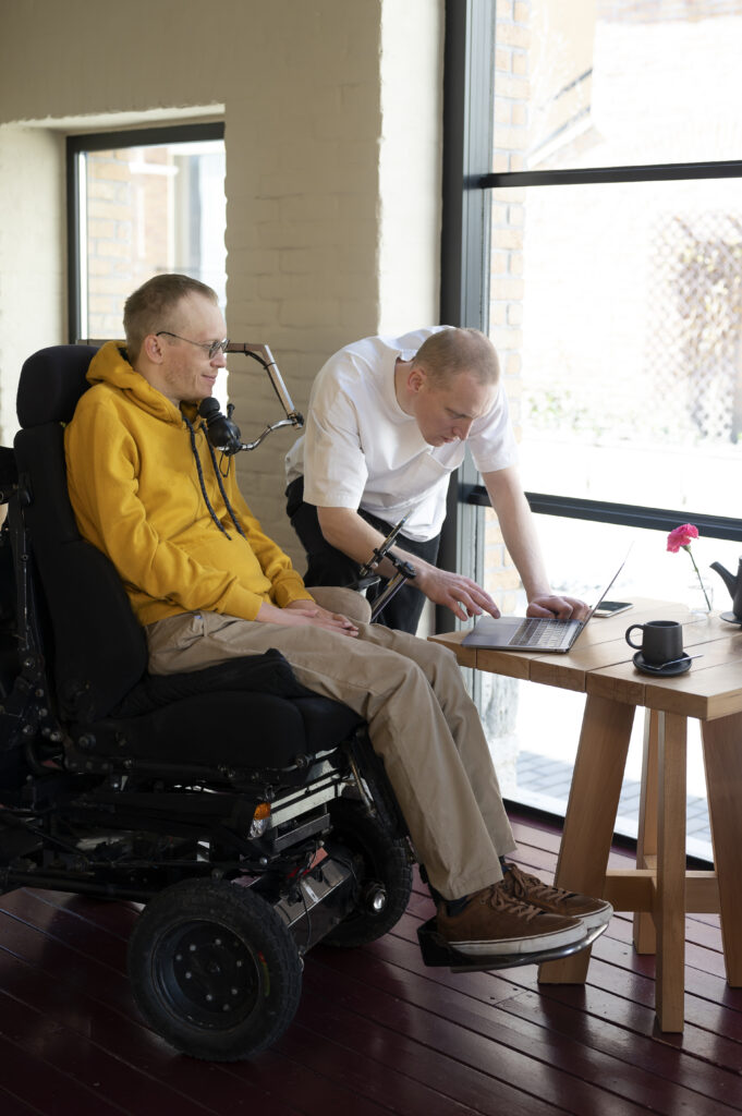 A man in a wheelchair and another man working on a laptop.