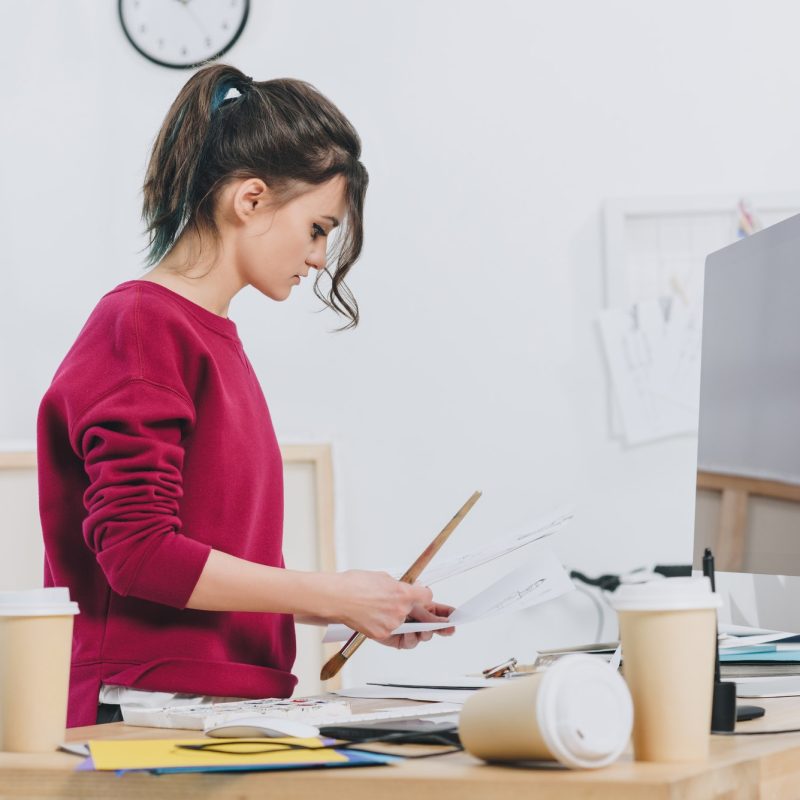 A woman is standing at her desk looking at papers.