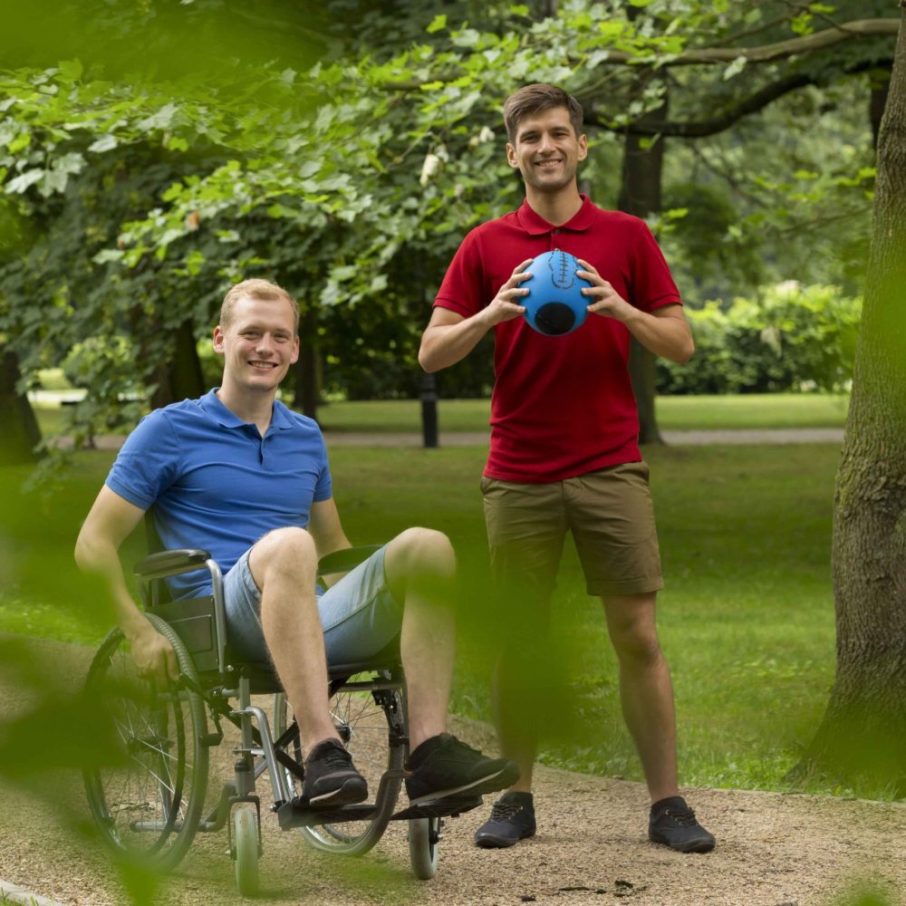 Two men in a park with one sitting on the ground and another holding a ball.