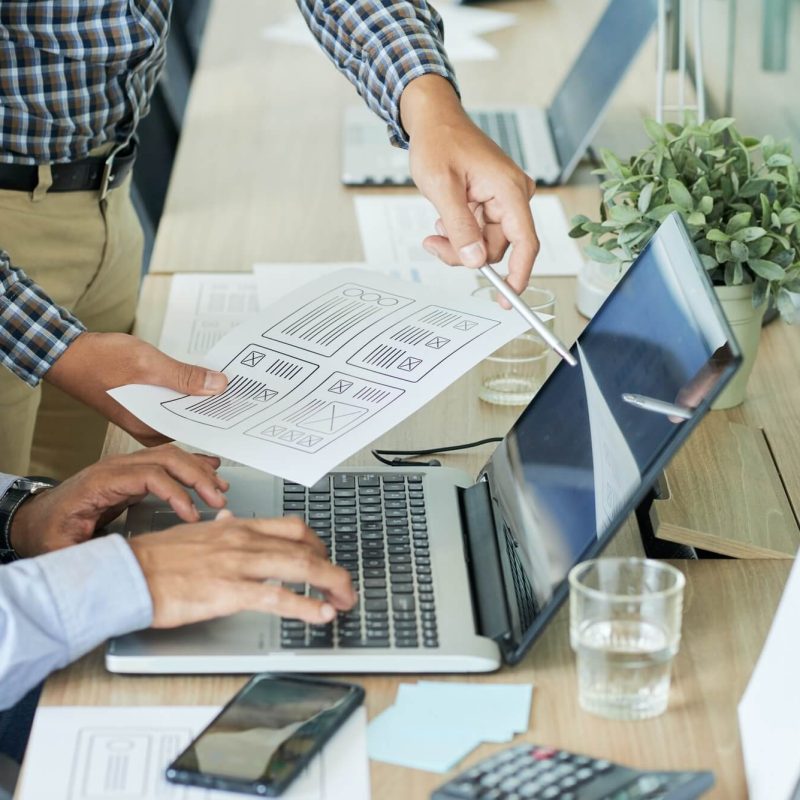 Two people are using a laptop and paper.